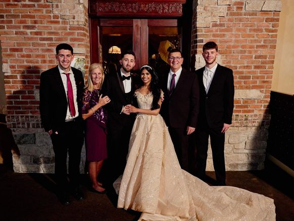 A bride and groom are posing for a picture with their family in front of a brick building.