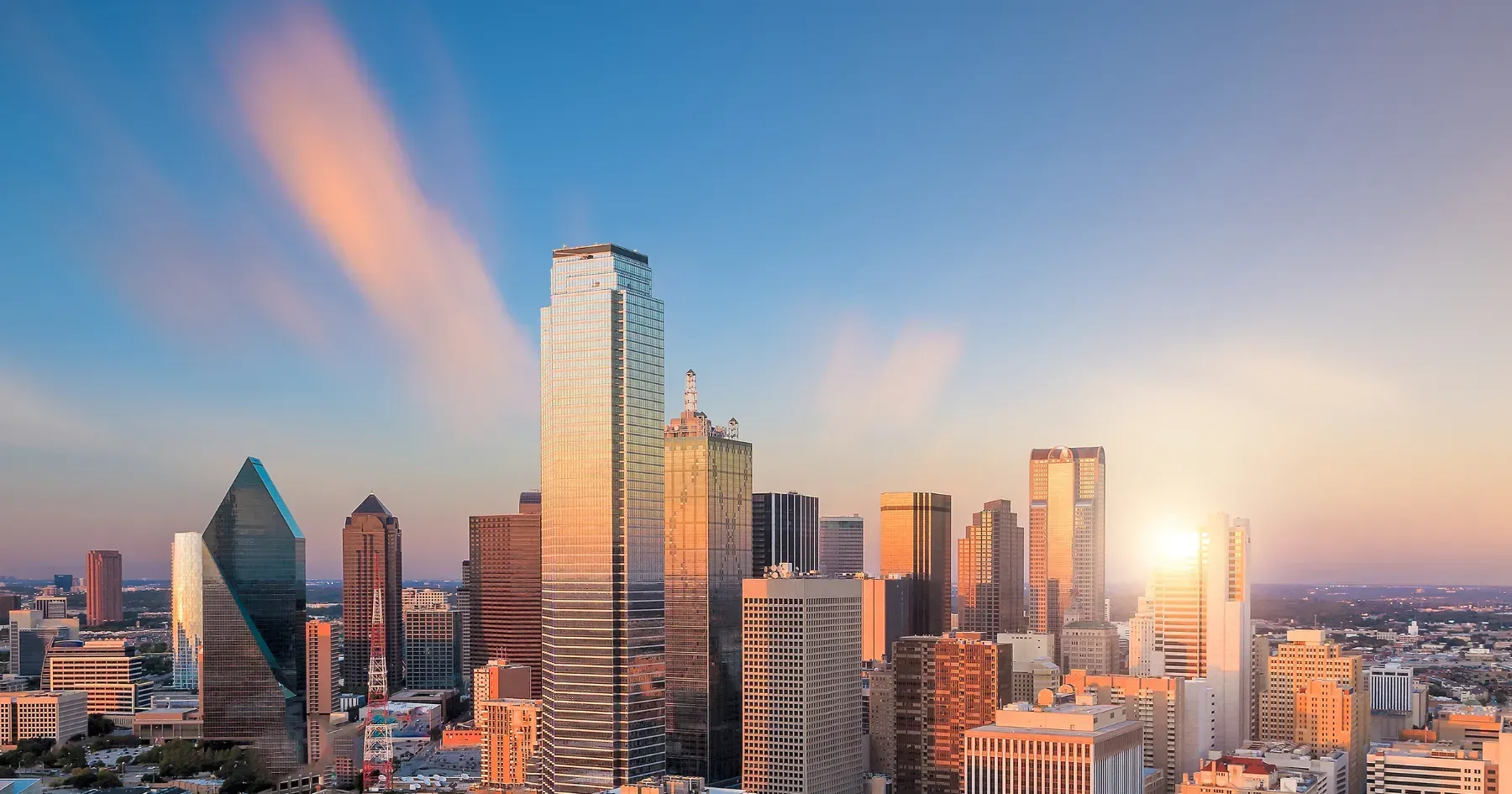 City skyline at sunset with tall glass skyscrapers glowing in warm light.