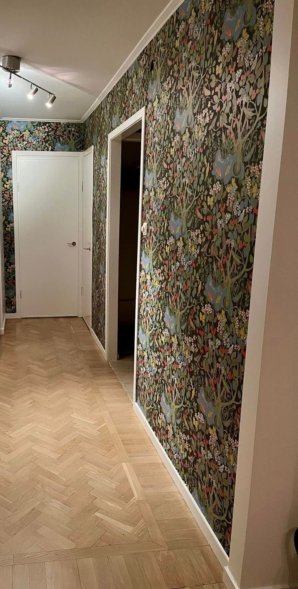 A hallway with a floral wallpaper on the walls and a wooden floor.