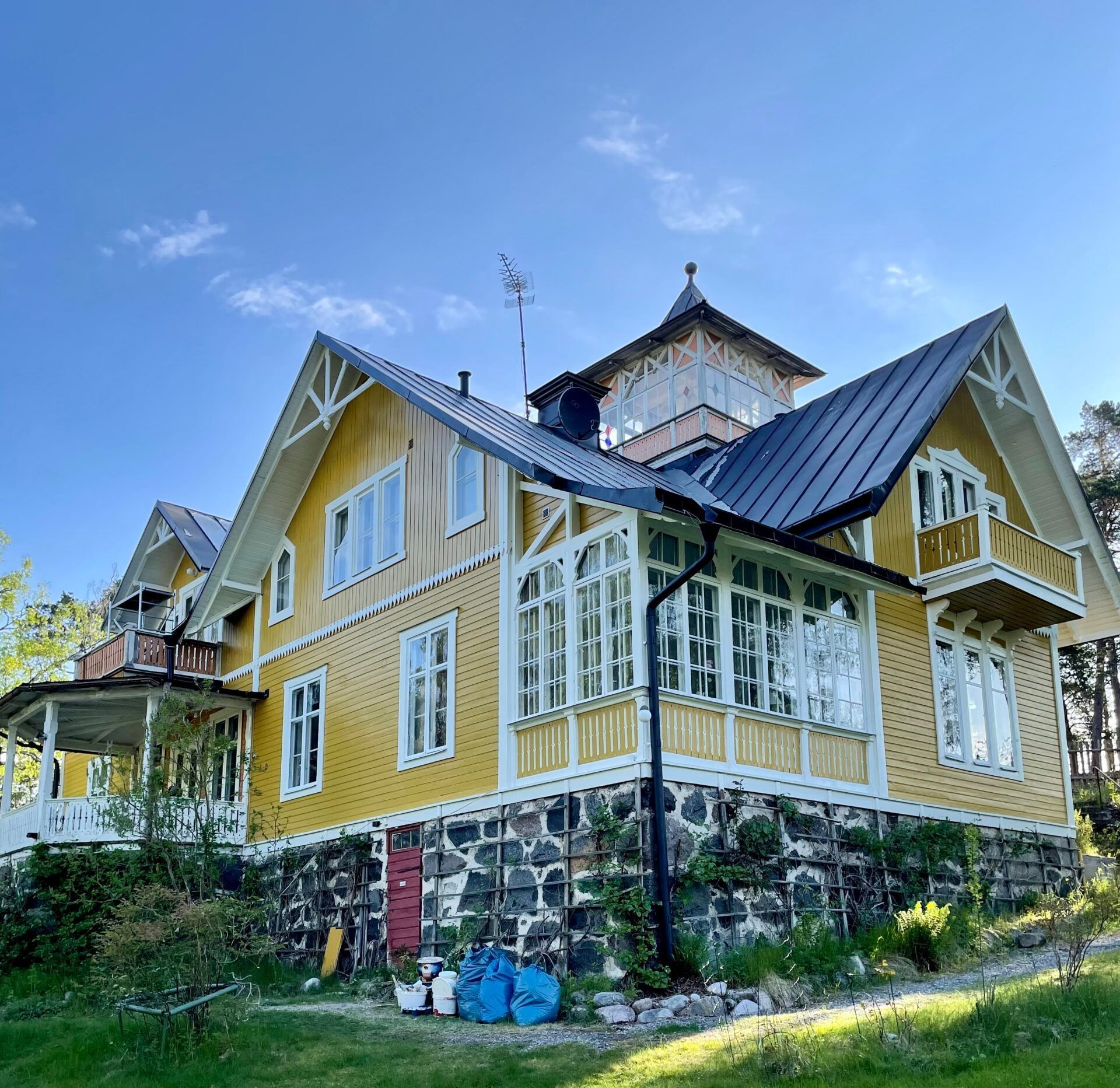 A large yellow house with a black roof is sitting on top of a hill.