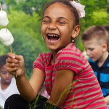 Child laughing and holding a flower outdoors, with two other children blurred in the background