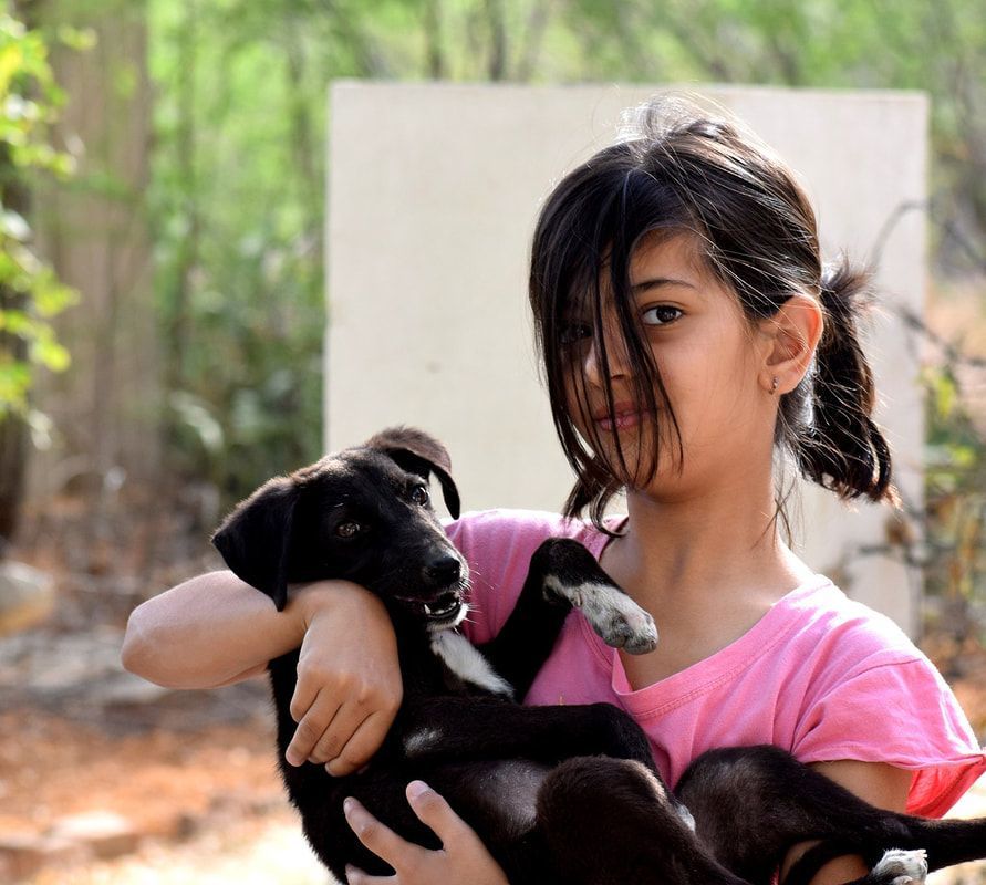 Woman in a pink shirt holding a black puppy outdoors