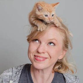 Blonde woman smiling with a small orange kitten on her head