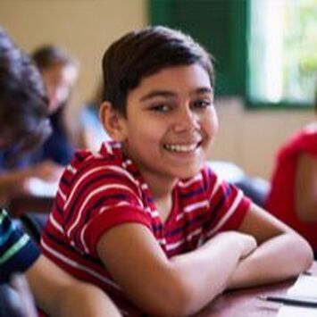 Smiling student in a red striped shirt leaning on a desk in a classroom