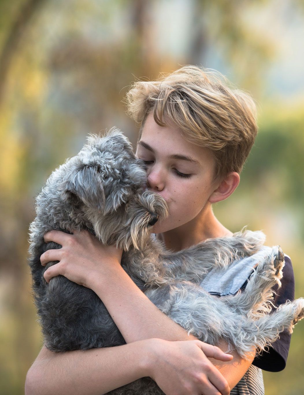 Person cuddling a gray cat outdoors, both nuzzling in soft sunlight