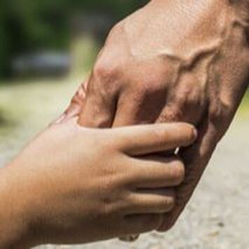 Adult hand holding a child’s hand outdoors on a sunlit path