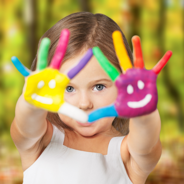 Child with painted hands, holding colorful handprints toward the camera against a blurred outdoor background
