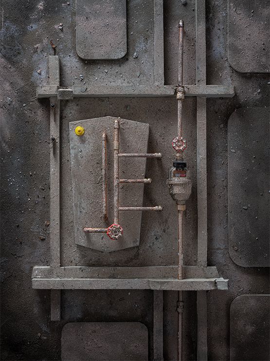 Grijze, gestructureerde industriële muur met koperen leidingen, afsluiters en een centrale tank.