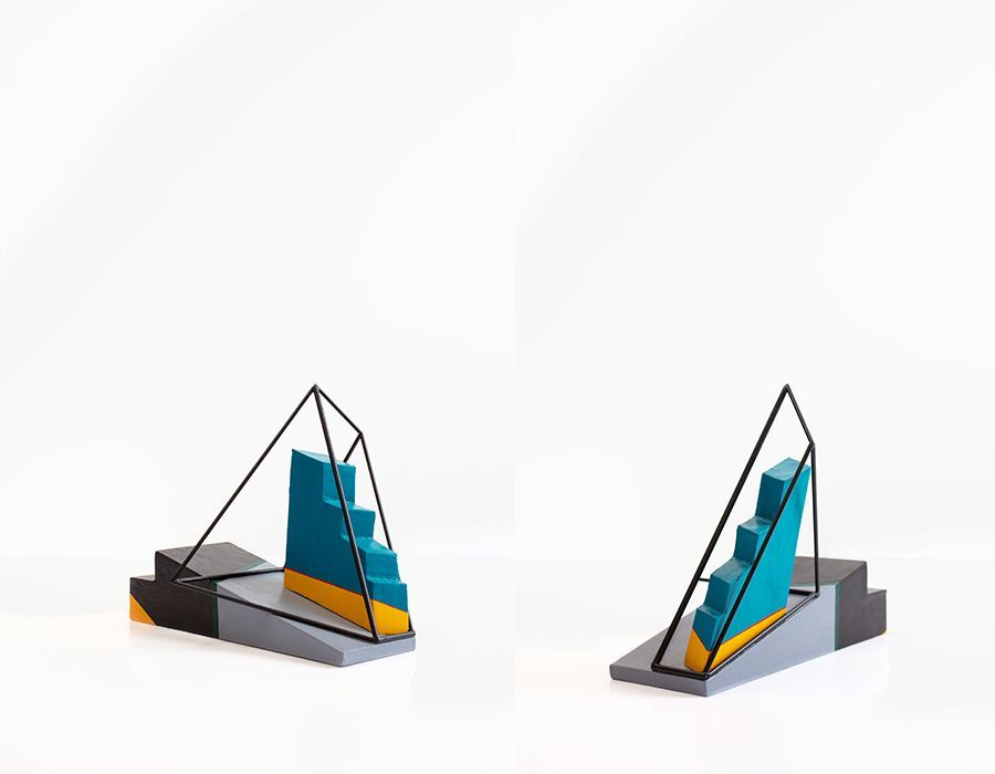 Twee abstracte sculpturen, elk met turquoise treden, gele accenten en zwarte draadframes, op een grijze sokkel.