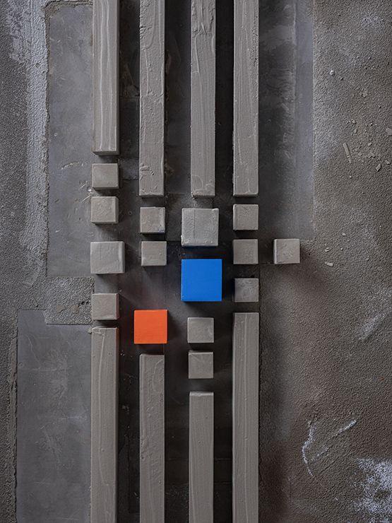 Grijze verticale balken en kleine kubussen omringen een blauw en oranje vierkant op een gestructureerde grijze achtergrond.