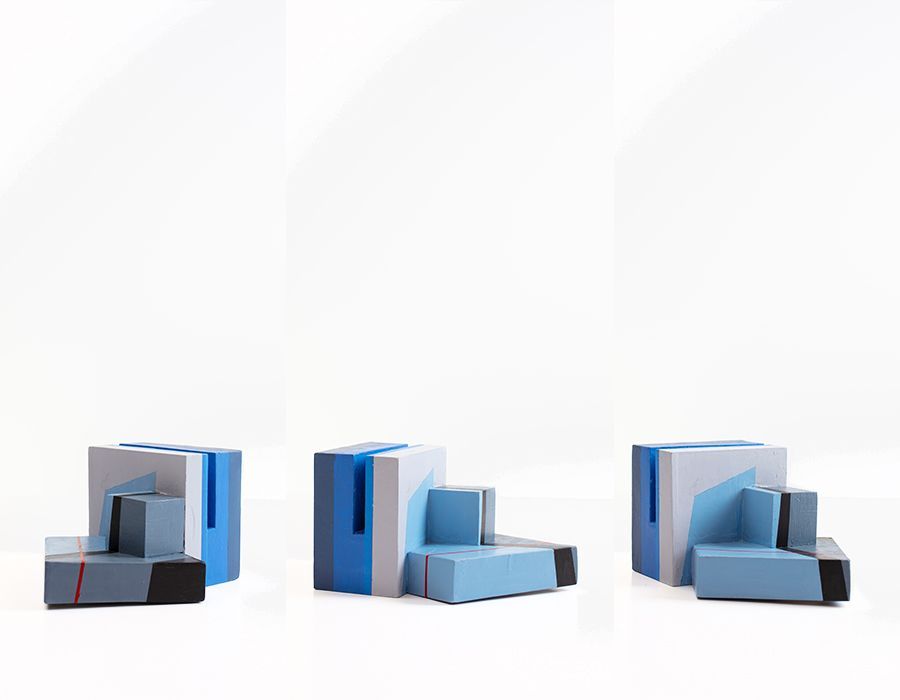 Drie geometrische sculpturen in blauw, wit en zwart tegen een witte achtergrond.