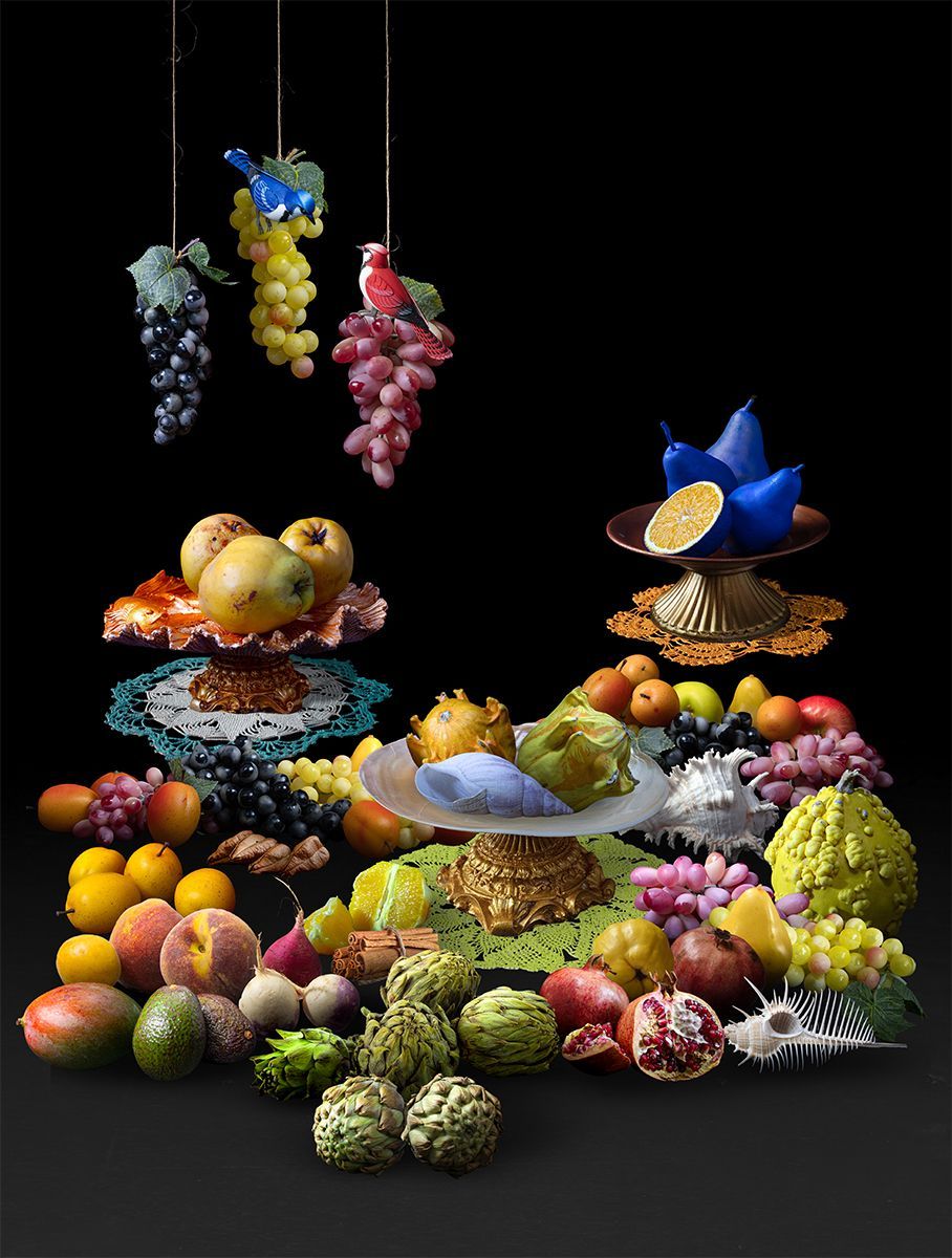 Stilleven met diverse kleurrijke vruchten: druiven, appels, peren, mango's, gerangschikt op sokkels en hangend.