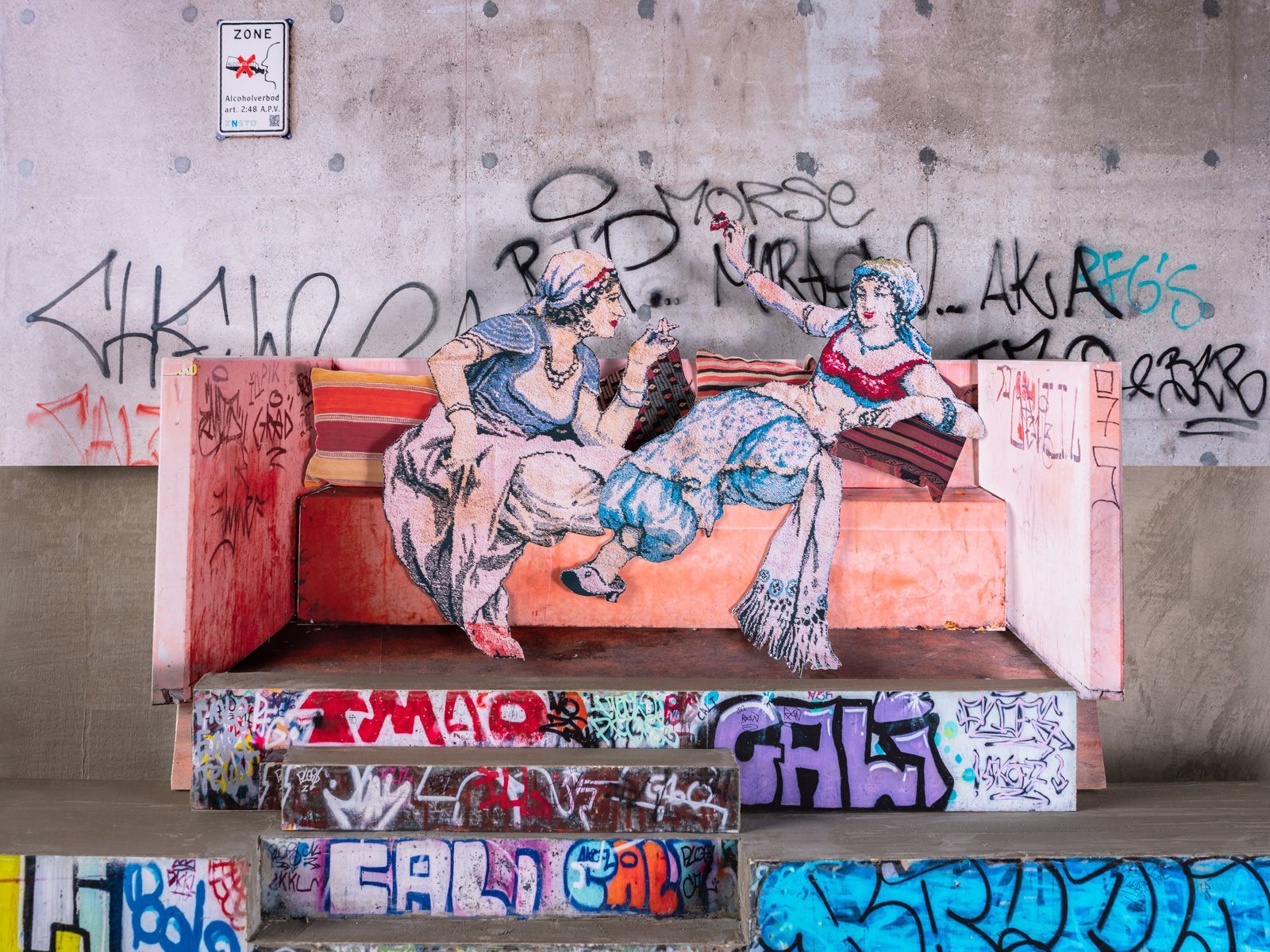 Graffiti van klassieke vrouwen op een roze bank in een betonnen skatepark.
