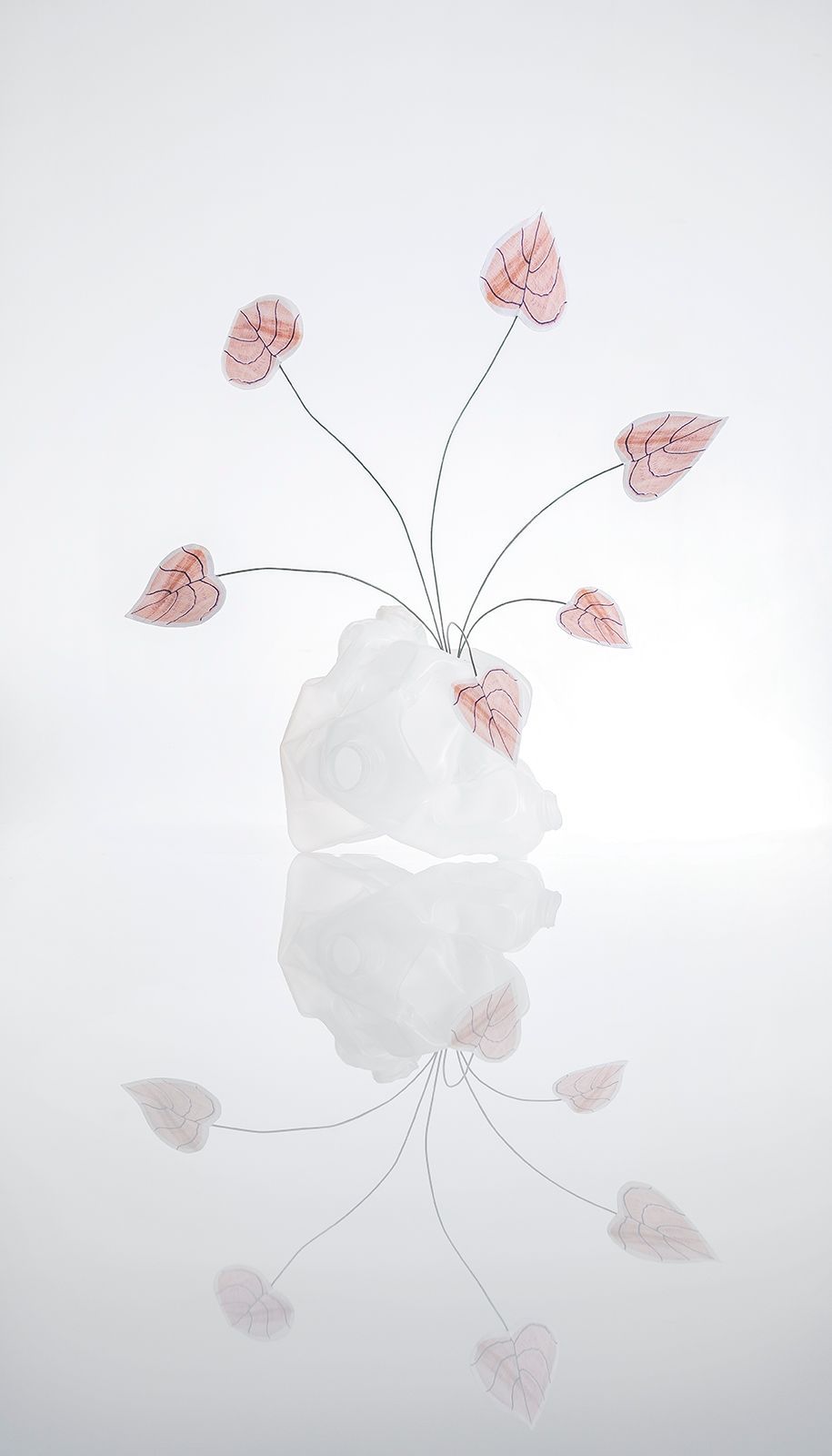 Kristallen sculptuur met roze bladeren en draadstelen, hieronder weerspiegeld.