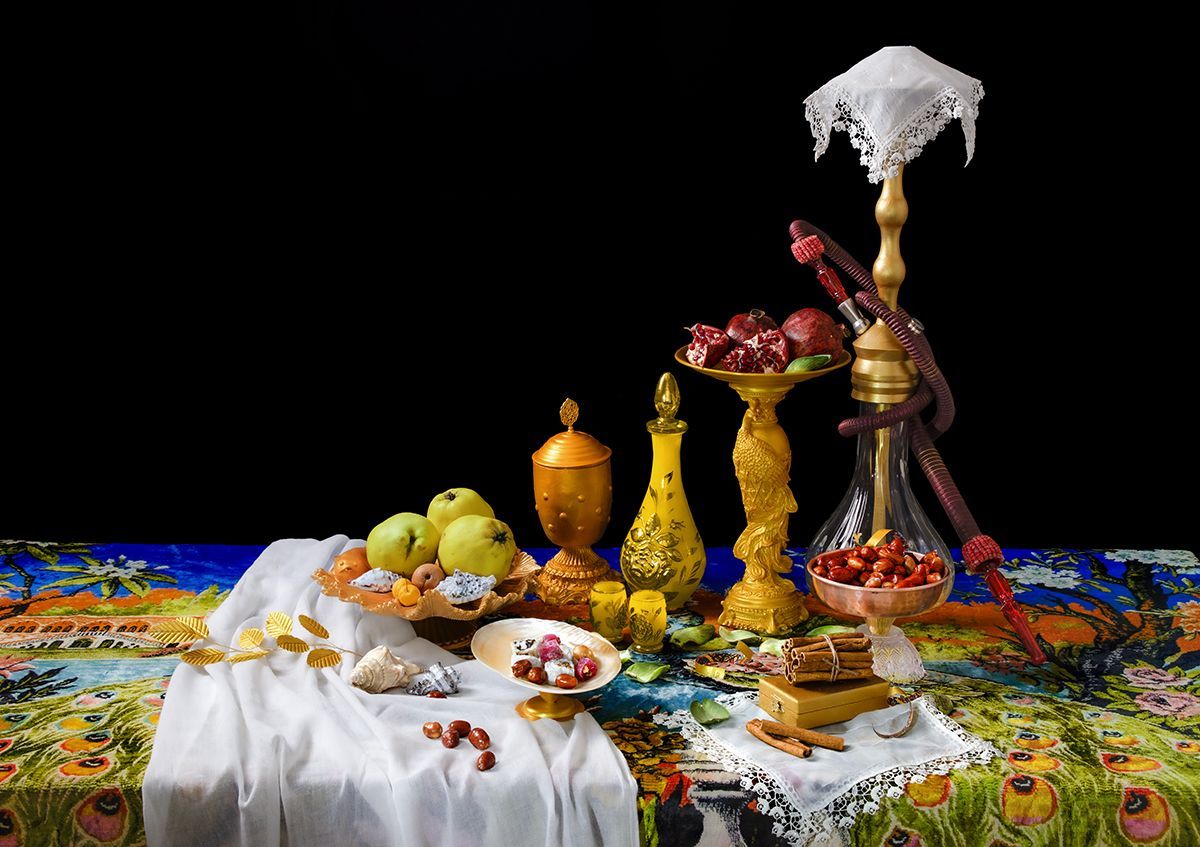 Stilleven met fruit, gouden vazen, waterpijp en een gedessineerd doek op een zwarte achtergrond.