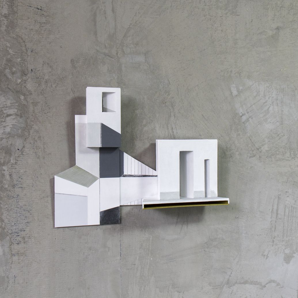 Abstracte wandsculptuur met witte, grijze en zwarte geometrische vormen, gemonteerd op een betonnen muur.