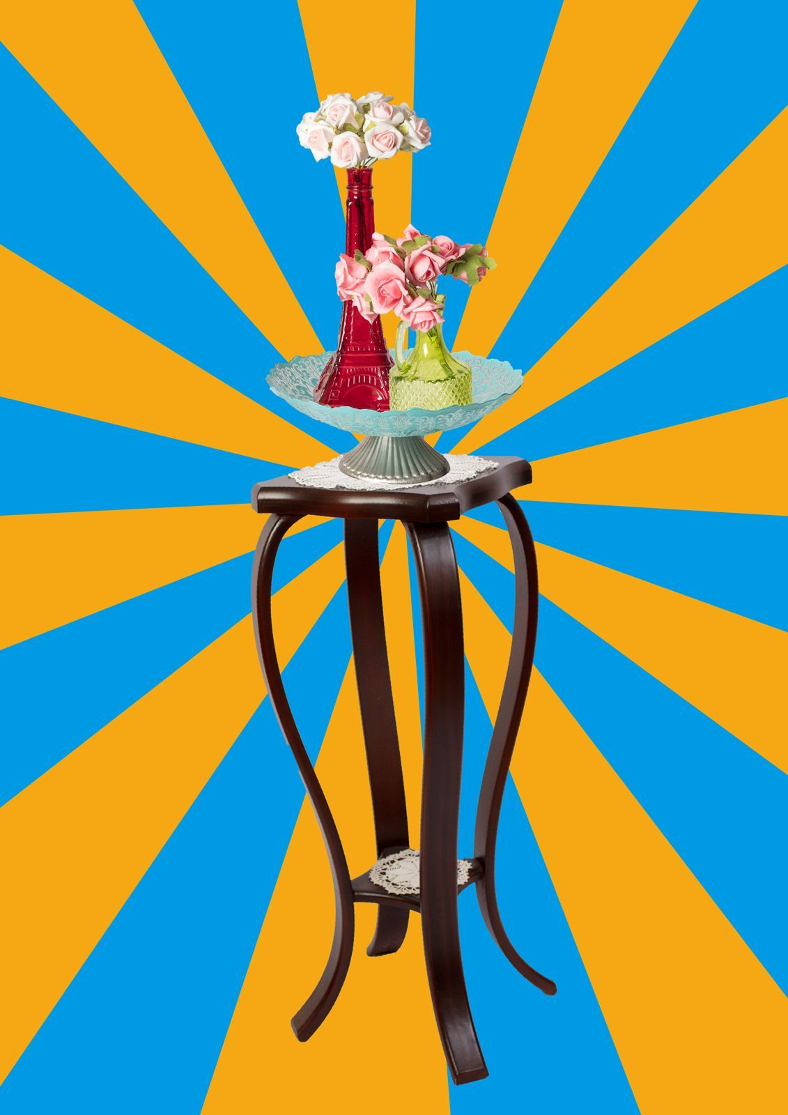 Een bloemstuk op een donkerhouten sokkel met een blauw-oranje zonnestralenachtergrond.