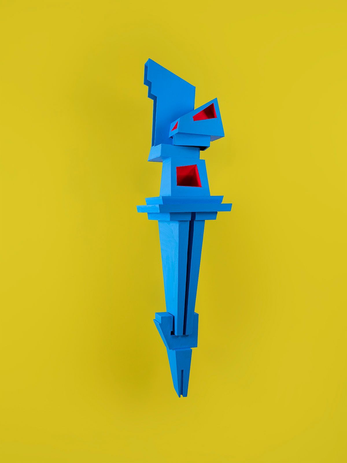 Blauwe, geometrische abstracte sculptuur op een gele achtergrond. Met rode accenten.