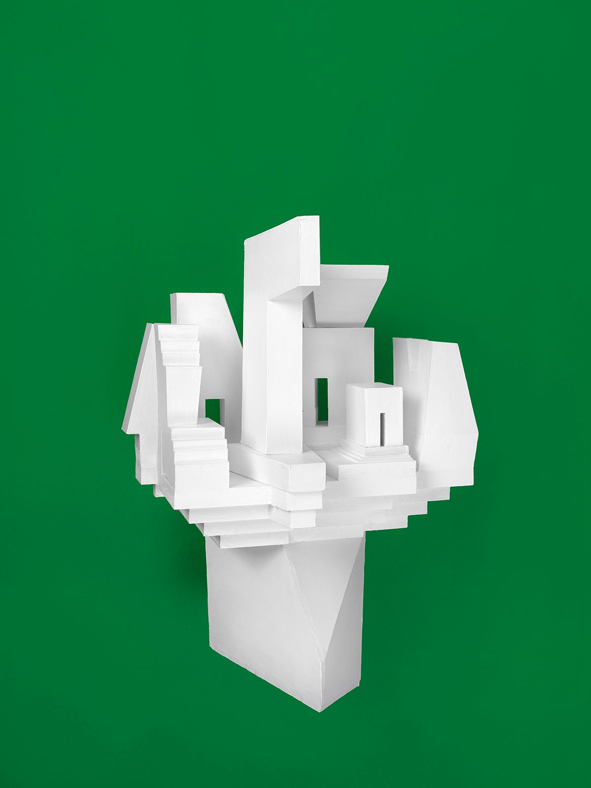 Witte geometrische sculptuur tegen een groene achtergrond, die doet denken aan een gestileerd stadsgezicht.