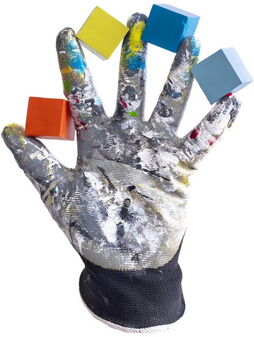 Een gehandschoende hand houdt vier kleurrijke houten blokken vast. De handschoen is bedekt met verf.