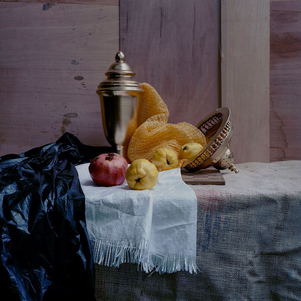 Stilleven met fruit, een gouden urn en gedrapeerde stof op een gestructureerde ondergrond.