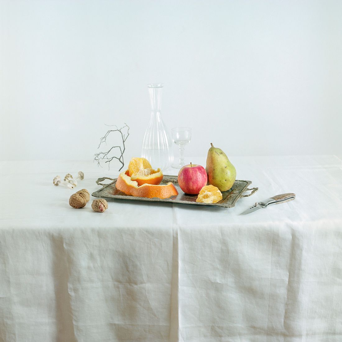 Stilleven: dienblad met fruit, fles, glas en mes op een wit tafelkleed.