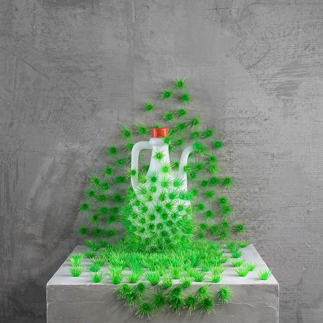 Een witte kan bedekt met groene, stervormige objecten op een grijs blok tegen een grijze muur met structuur.
