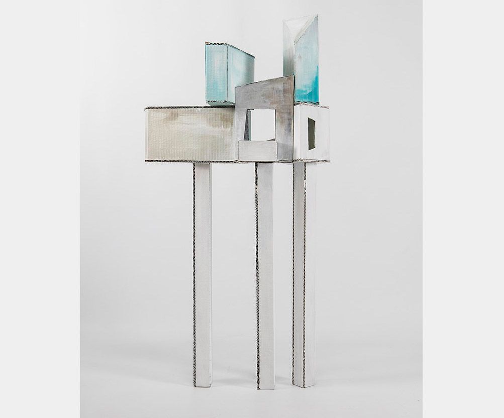 Abstracte sculptuur bestaande uit gestapelde, geometrische vormen op hoge, dunne poten; beschilderd in zilver, wit en turquoise.