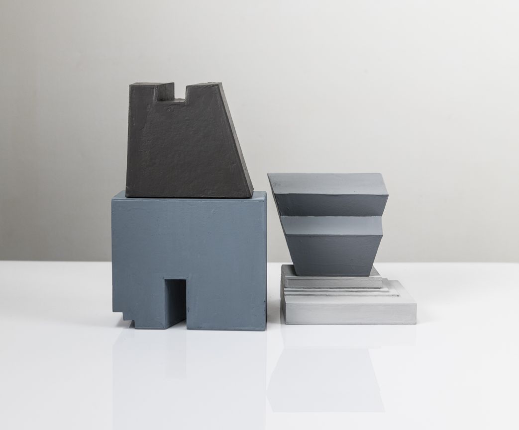 Drie abstracte sculpturen in grijs en blauw op een witte ondergrond.