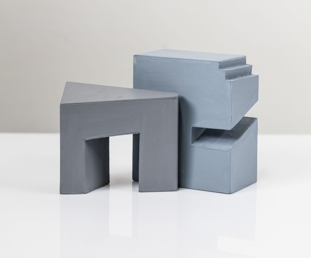 Grijze en blauwe geometrische sculptuur op een witte ondergrond.