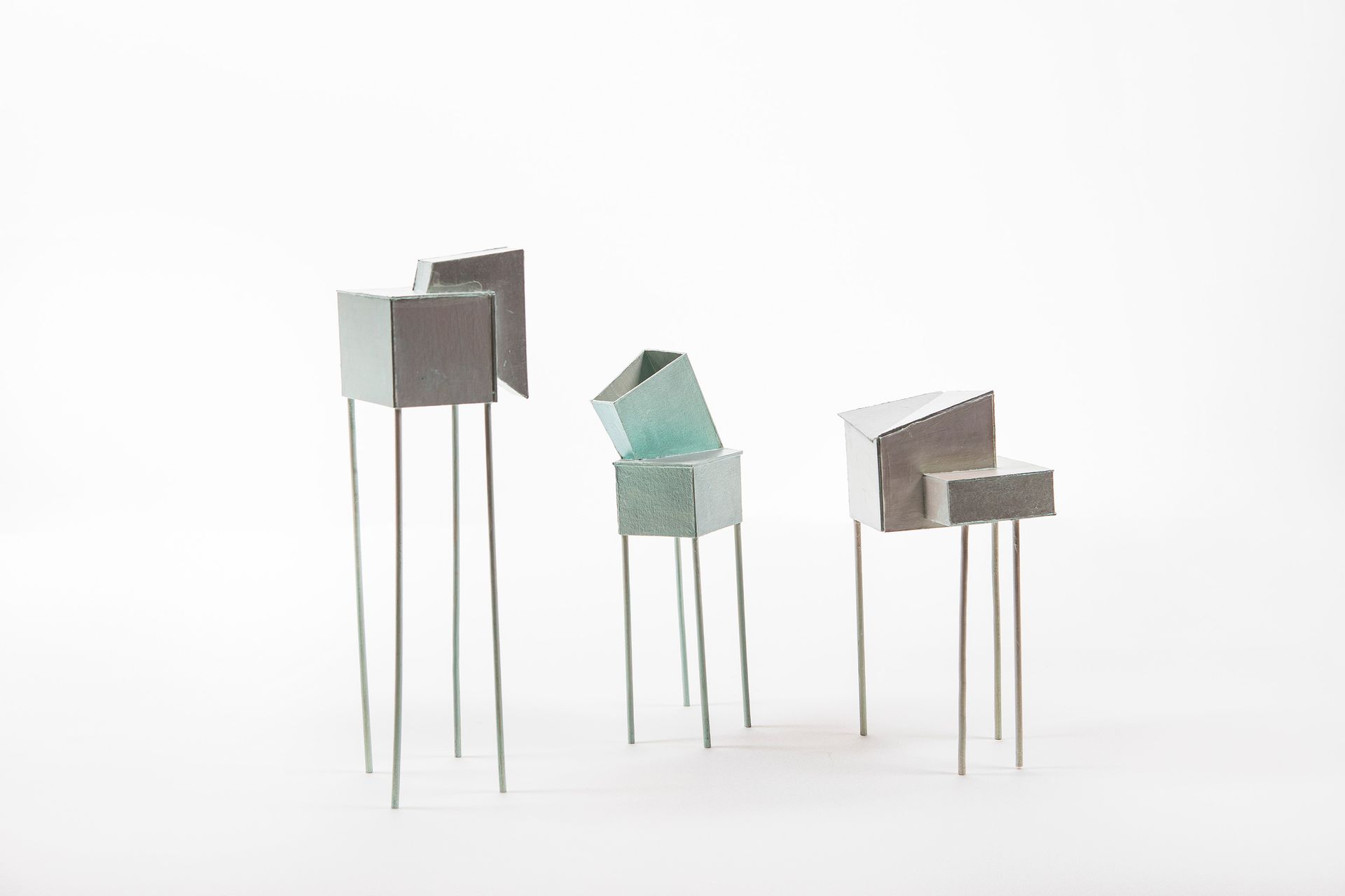 Drie abstracte metalen sculpturen met hoekige bovenkanten en dunne poten op een witte achtergrond.