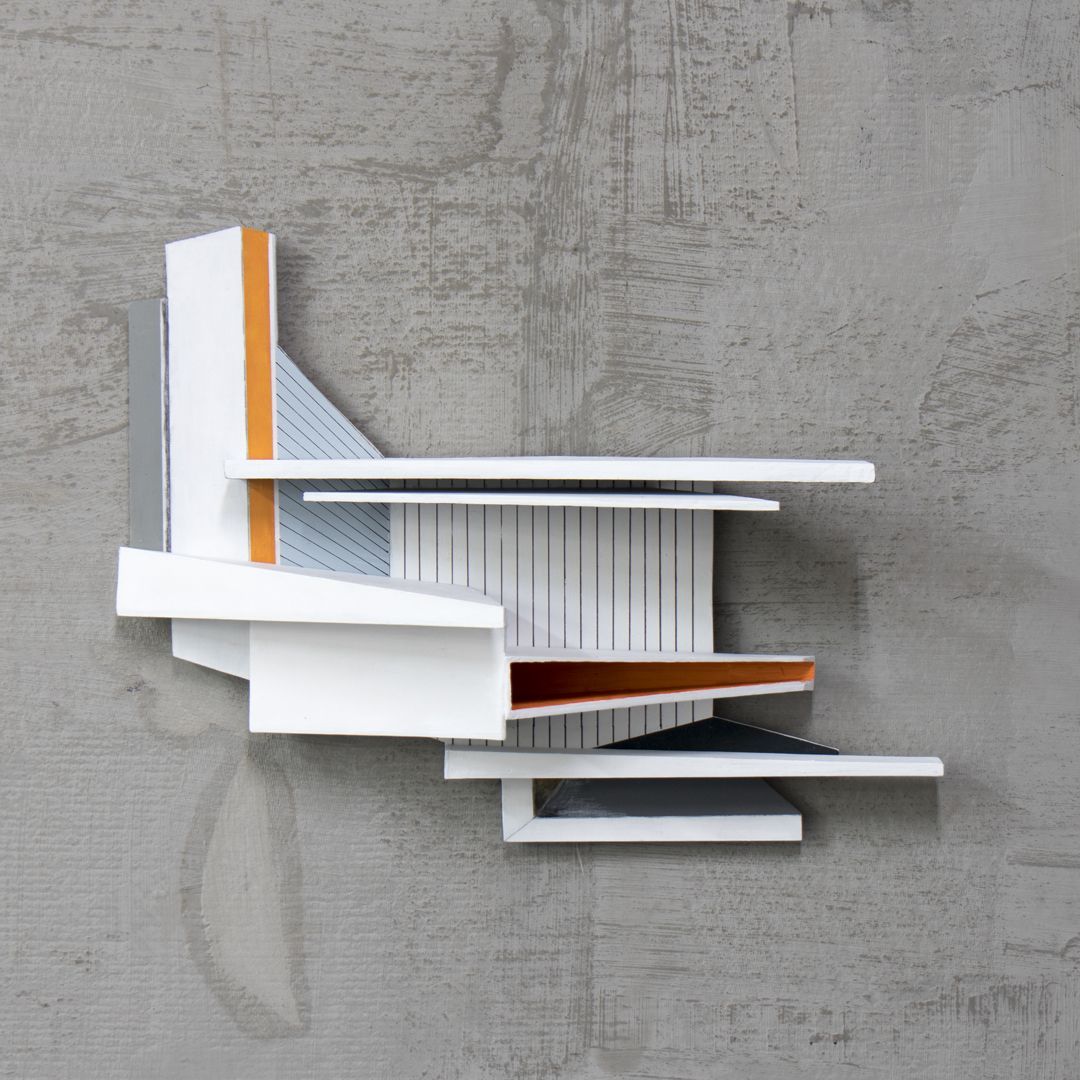 Abstracte, geometrische sculptuur gemonteerd op een grijze muur. Witte, oranje en grijze geschilderde vormen overlappen elkaar.