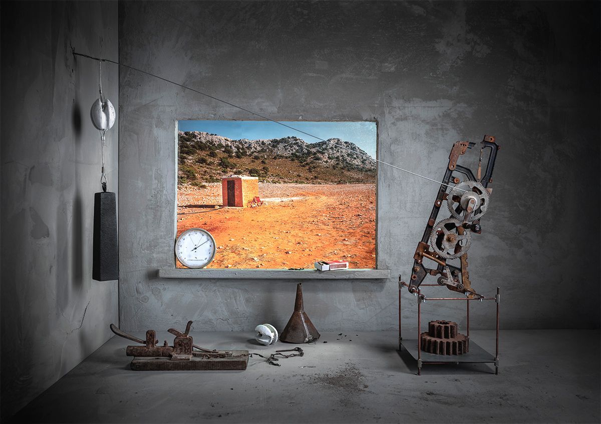 Kamer met raam; woestijnlandschap buiten. Klok, mechanische apparaten en objecten op de oppervlakken.