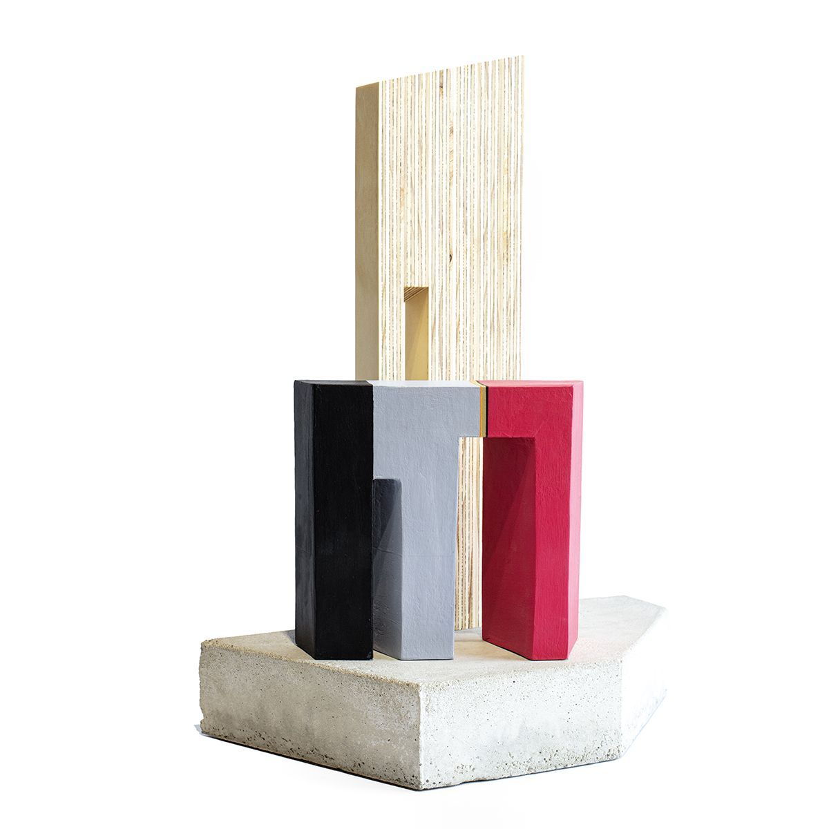 Abstracte sculptuur: blokken zwart, grijs en rood op een betonnen sokkel met een lichtbruin houten paneel op de achtergrond.