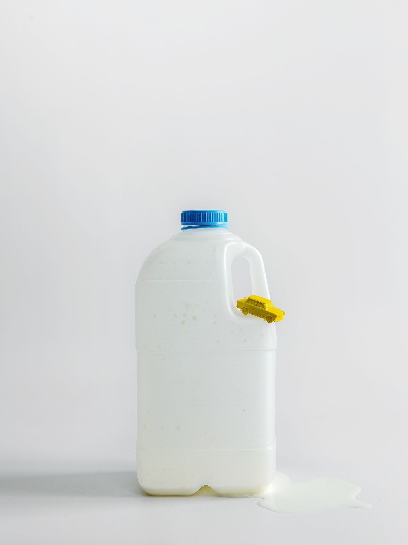 Een doorzichtige melkkan met blauw deksel, geel label aan het handvat en een plasje gemorste melk.