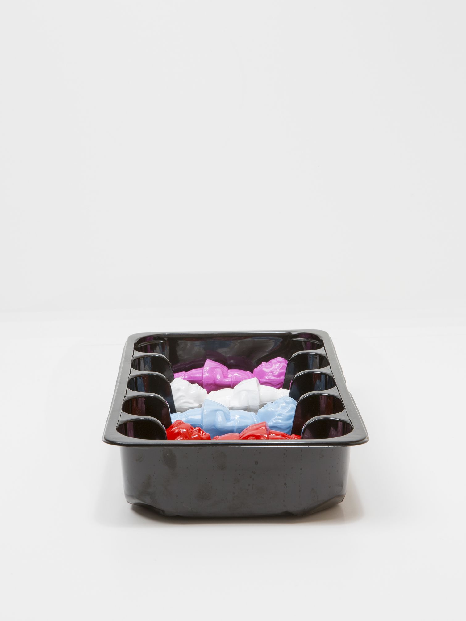 Zwarte plastic schaal gevuld met kleurrijke, kleine plastic voorwerpen tegen een witte achtergrond.