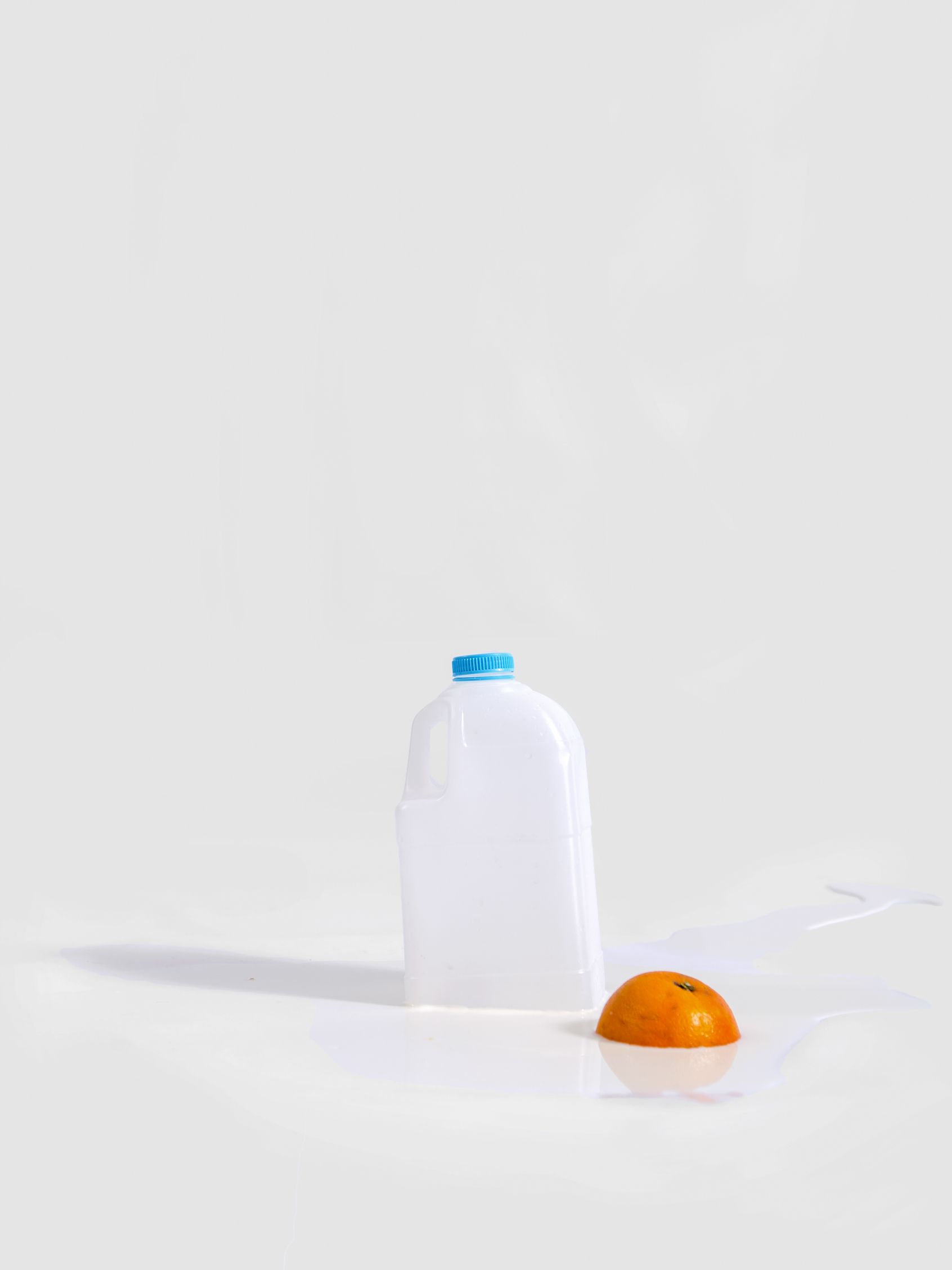 Witte fles met een blauwe dop en een halve sinaasappel op een witte achtergrond.