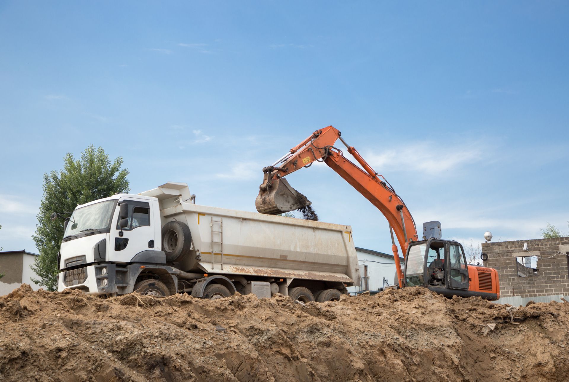 An excavator loading dirt into a dump truck on a construction site; blue sky background. An excavator loading dirt into a dump truck on a construction site; blue sky background.