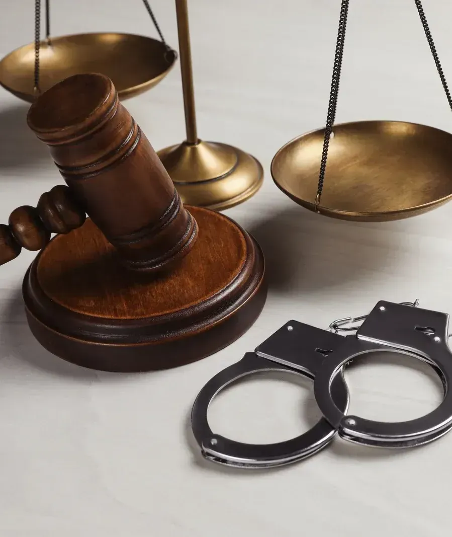 A pair of handcuffs sitting next to a judge 's gavel and scales of justice