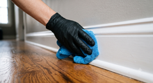 Person steam-cleans a beige couch with a handheld upholstery cleaner.
