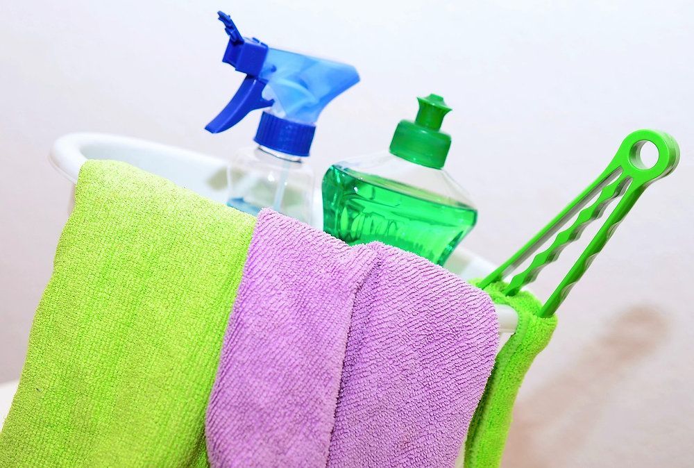 Colorful cleaning cloths with spray bottles and a green cleaning tool on a white background