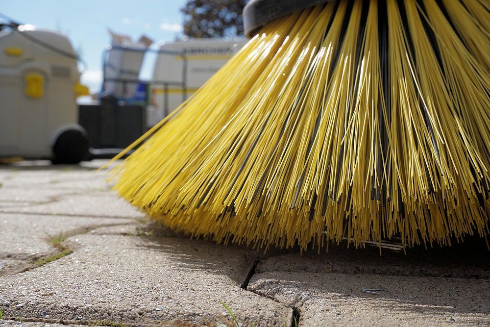 Close-up of a yellow broom sweeping a paved sidewalk outdoors