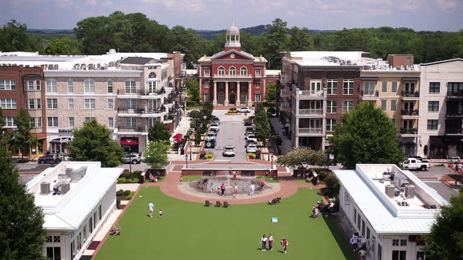 Aerial view of a town square with a green lawn, fountain, and a domed building at the far end.