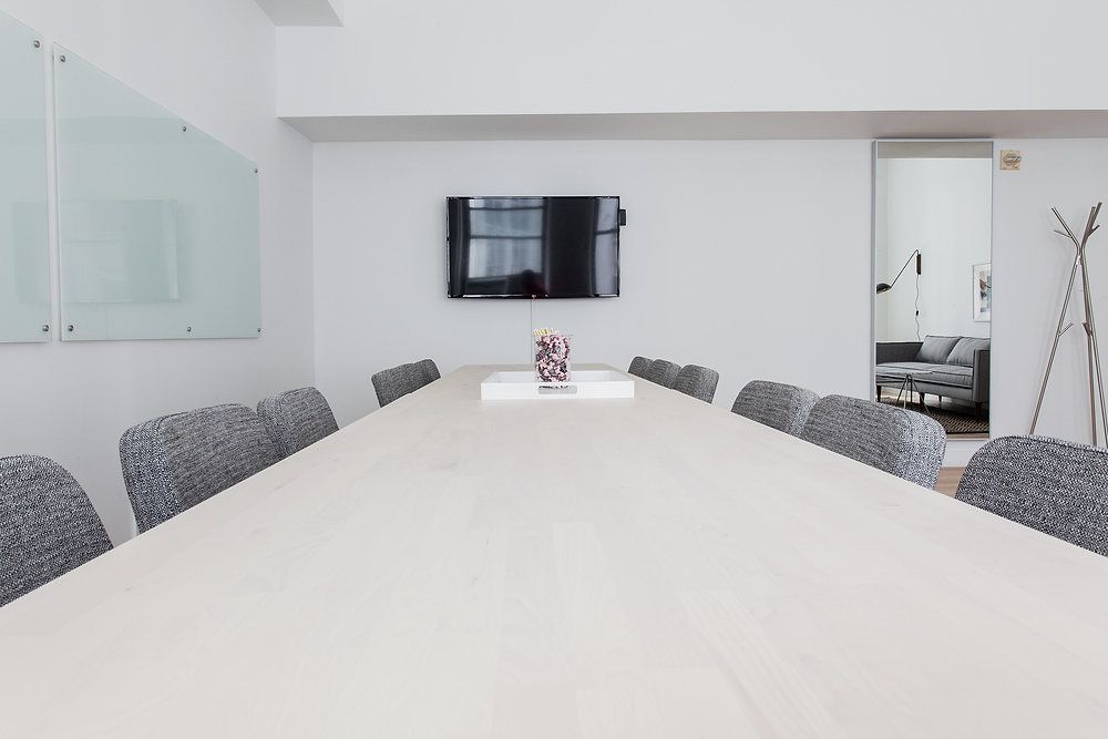 Modern conference room with a long white table, gray chairs, wall-mounted TV, and glass cabinets