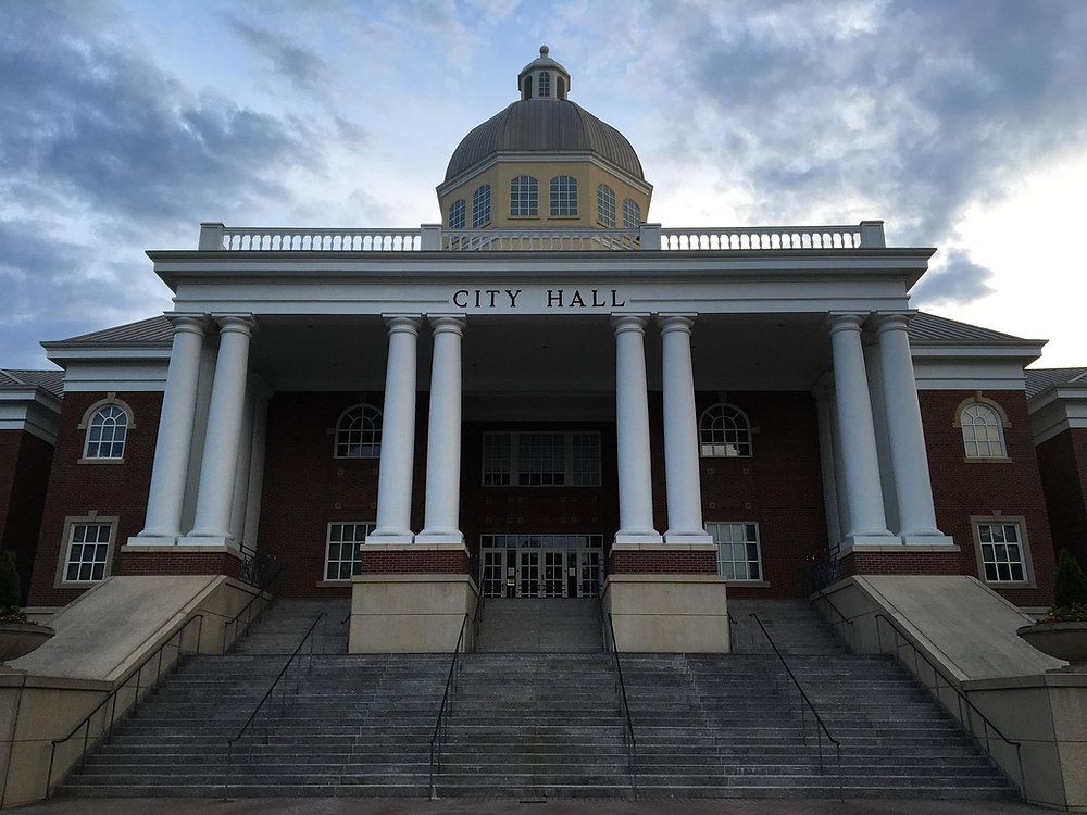 City Hall building with white columns, red brick facade, and steps leading to the entrance at dusk