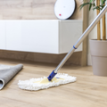 Mop cleaning a hardwood floor in a bright living room with a potted plant and cabinet nearby