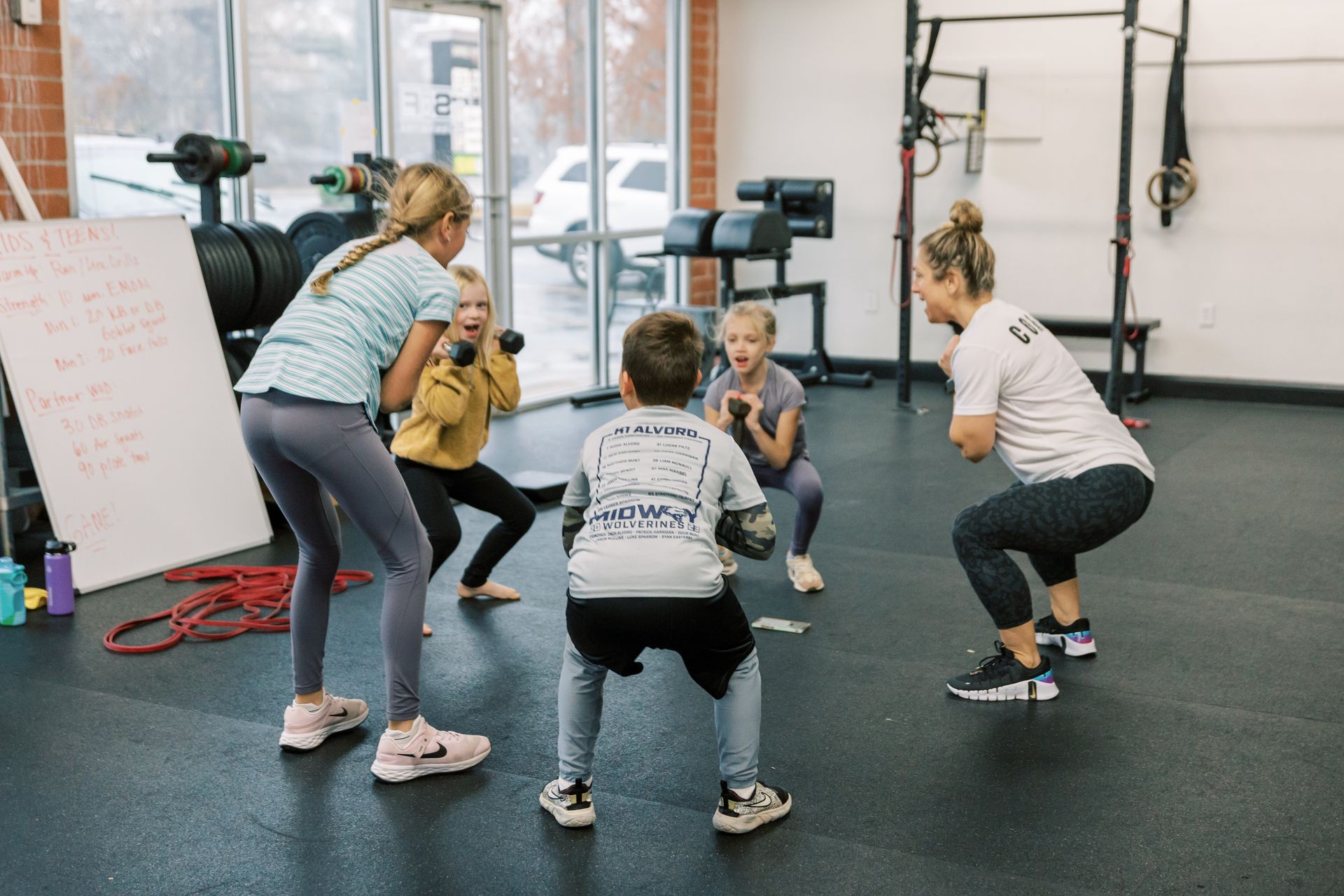 Fitness class doing squats in a gym with a trainer nearby