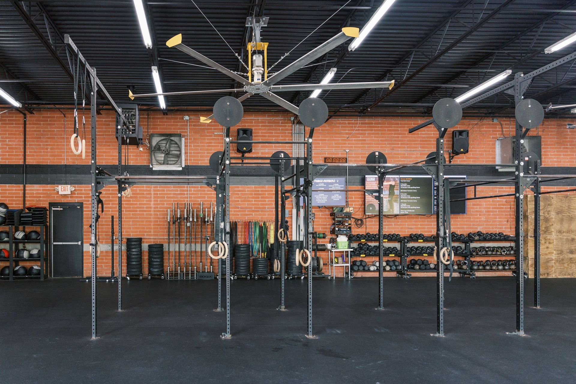 Empty CrossFit gym with pull-up rigs, black flooring, and orange brick walls