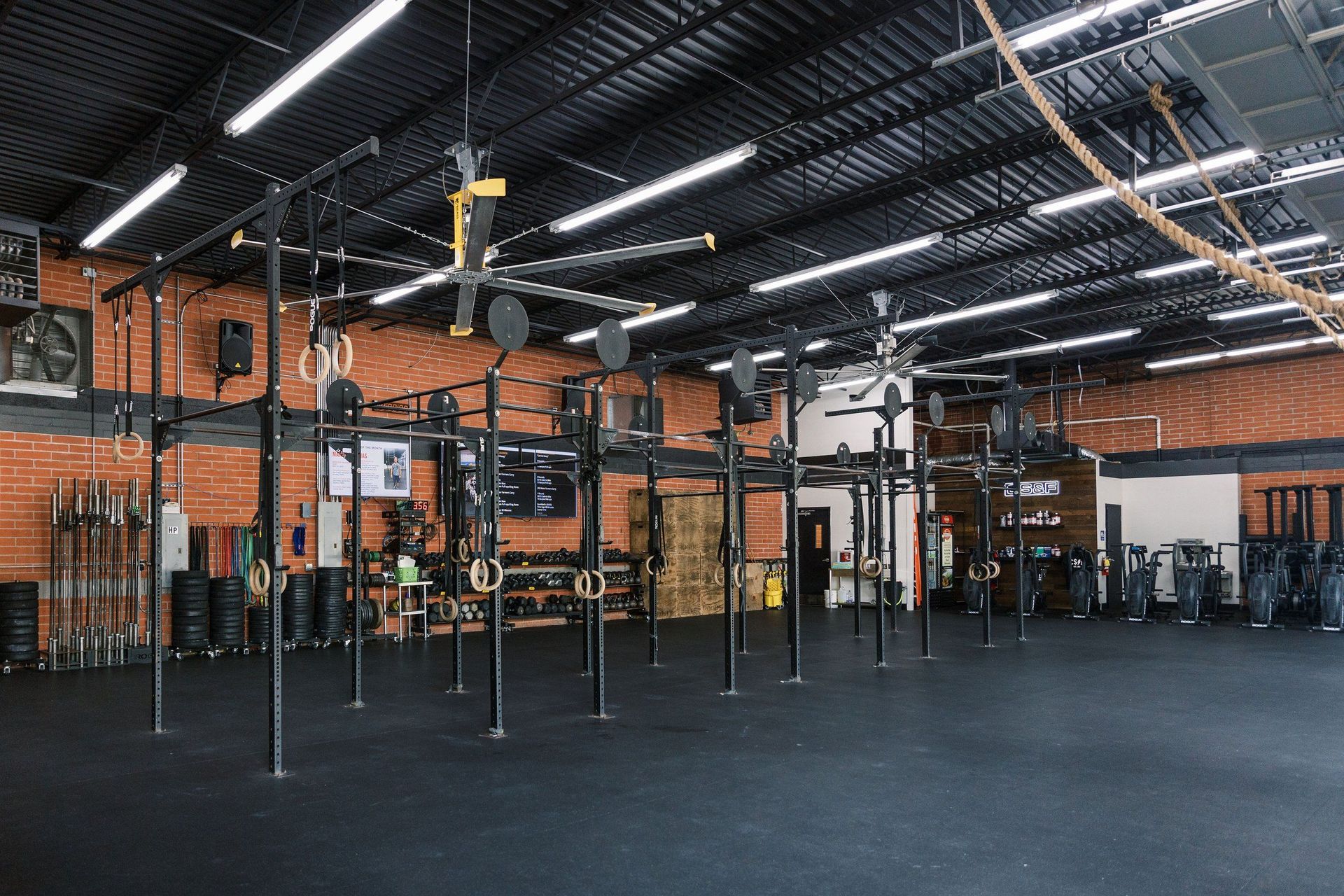 Empty CrossFit gym with pull-up rigs, black flooring, orange brick walls, and overhead lights.