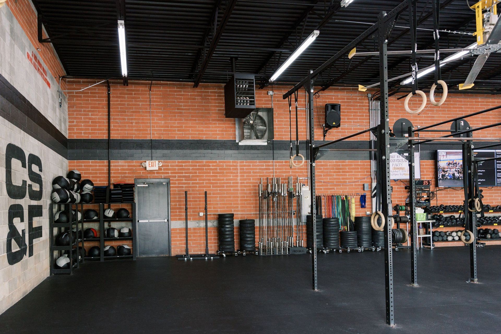Empty CrossFit gym with black rig, brick walls, and stacked weights under high ceiling
